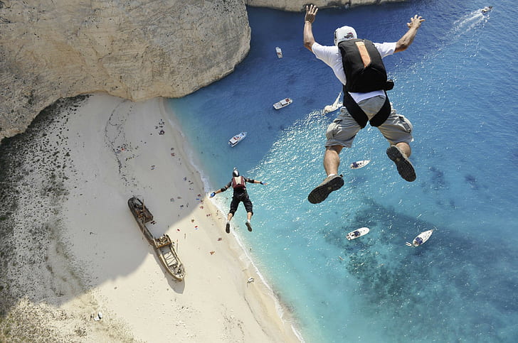 helmet  sunlight  sports  men  sand  sea  birds eye view  parachutes  Greece  beach  boat  rock  jumping