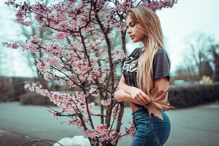 women's gray shirts, woman in black crew-neck t-shirt and blue denim bottoms standing beside pink flowering tree during daytime