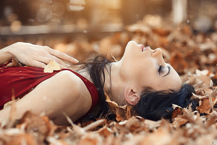 women's red tank top, woman in maroon sleeveless dress laying down on a bunch of brown leaves