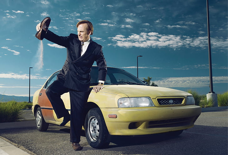 man in black suit jacket and dress pants holding brown loafers standing beside yellow car under blue sky during day time, HD wallpaper