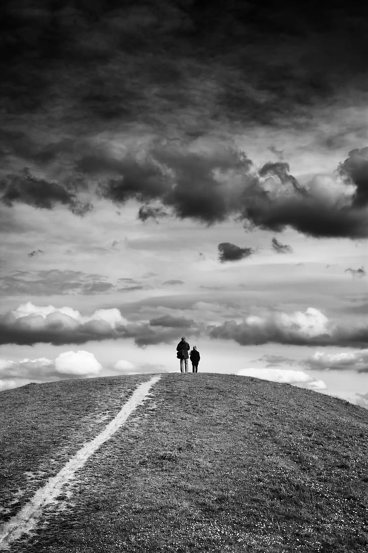 grayscale photography of man and child standing front of clouds on mountain