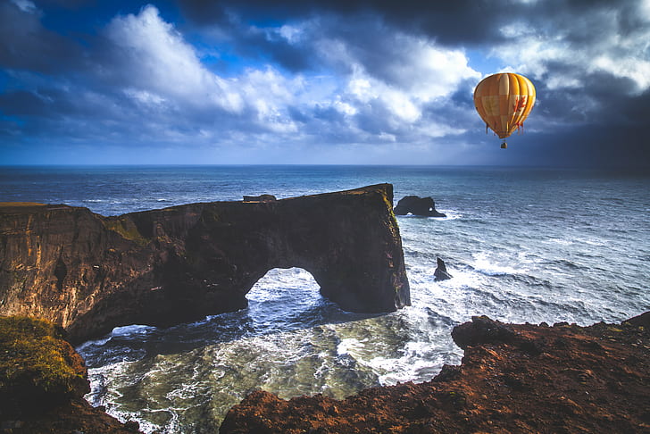 hot air balloon floating above sea near boulders, Dyrhólaey
