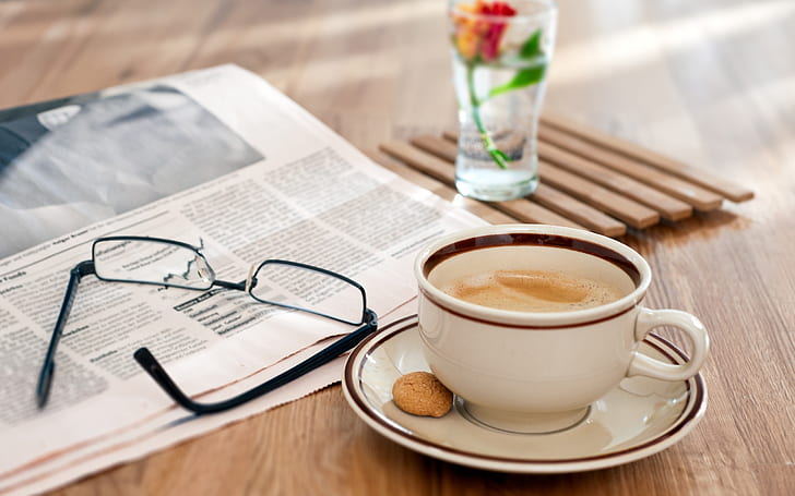 Still life, wooden table, glasses, newspaper, coffee, white ceramic teacup and black frame clear lens eyeglasses