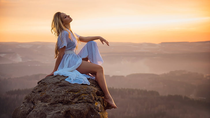 woman wearing white dress, woman wearing white dress sitting on rock formation during golden hour