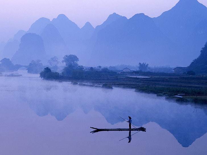man riding canoe on body of water near mountain range, china