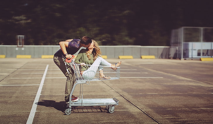 man kissing woman riding on white shopping cart during daytime