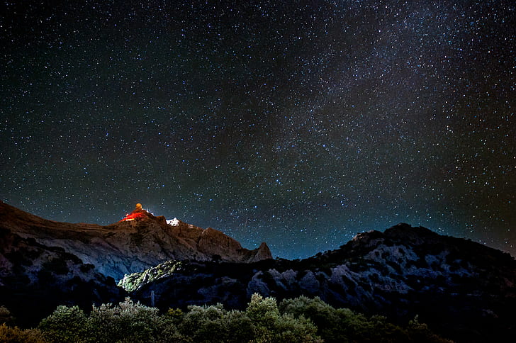 low angle photography of stars, mountains and green leafy trees