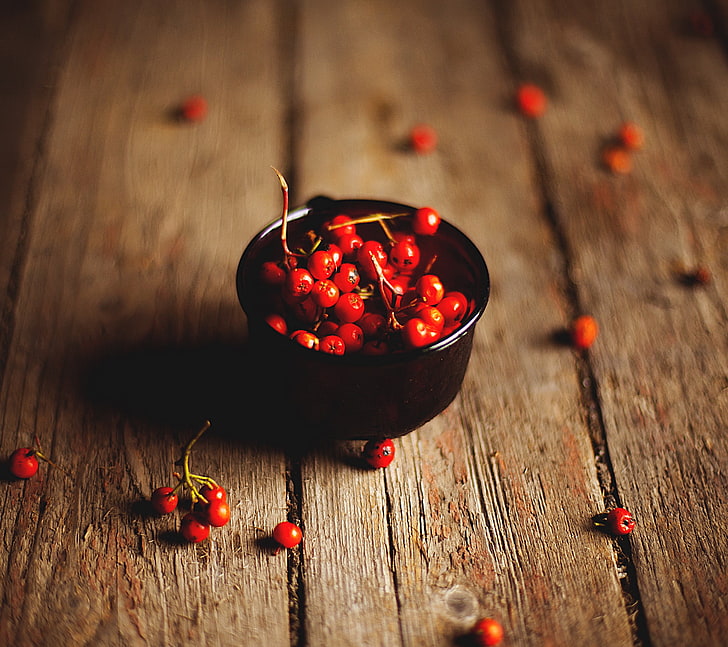 selective focus photo of bowl of cherries, wooden surface, rose hip