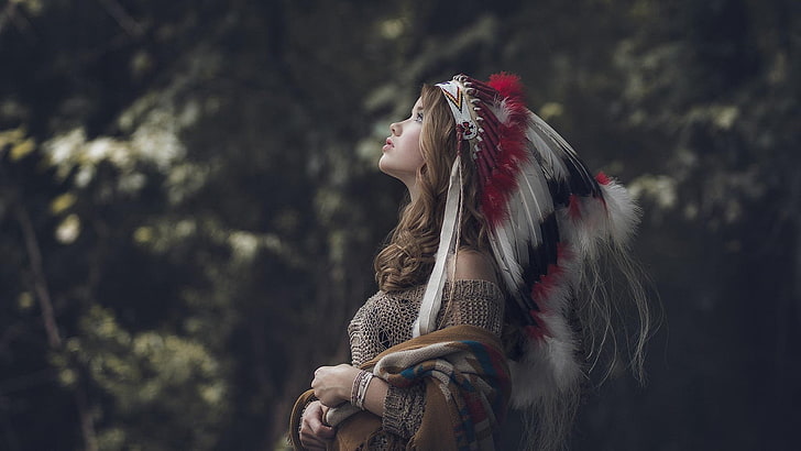 women's gray native American costume, woman in white, red, and black feather headdress looking up