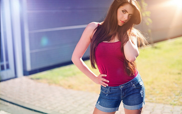 woman in red camisole and blue denim short shorts stands near grass field at night