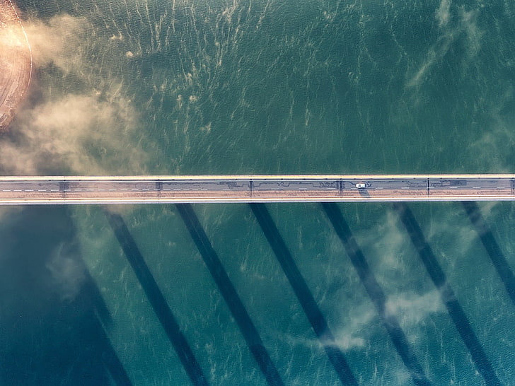 gray concrete bridge over body of water, car, sea, clouds, shadow