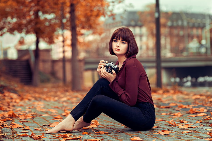 women's maroon long-sleeved shirt and black pants, woman in maroon long-sleeved top and blue jeans sitting on ground surrounded by dried leaves tilt shift photography