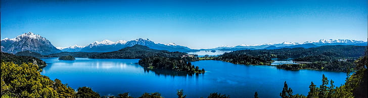 panoramic photography of body of water surrounded by trees and snowy mountains under clear blue sky during daytime