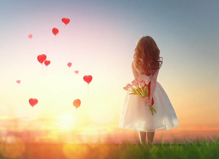 girl holding pink tulip flowers while staring at balloons in the sky