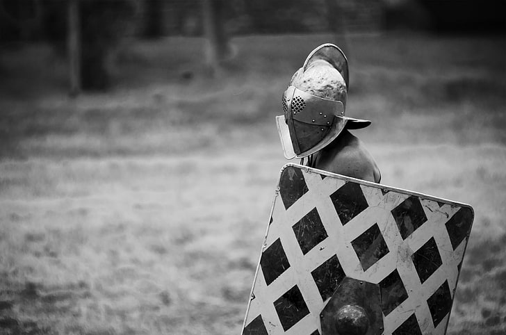grayscale photo of man wearing knight armor helmet and shield