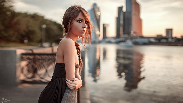 women's black strapless dress, woman in black and grey dress standing near calm body of water and concrete buildings during daytime