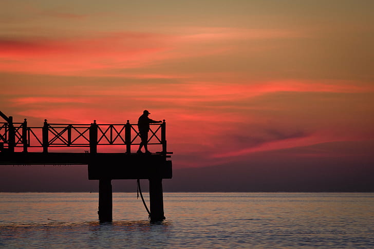 silhouette photo of person standing on dock, amanecer, cielo