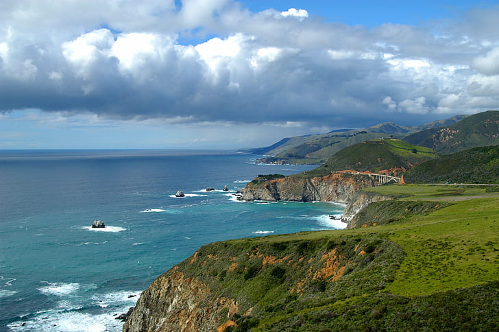 photography of cliffs near ocean under blue and white cloudy sky during daytime