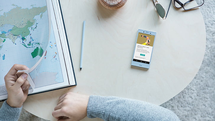 person wearing gray sweater sitting in front table holding world map print beside smartphone