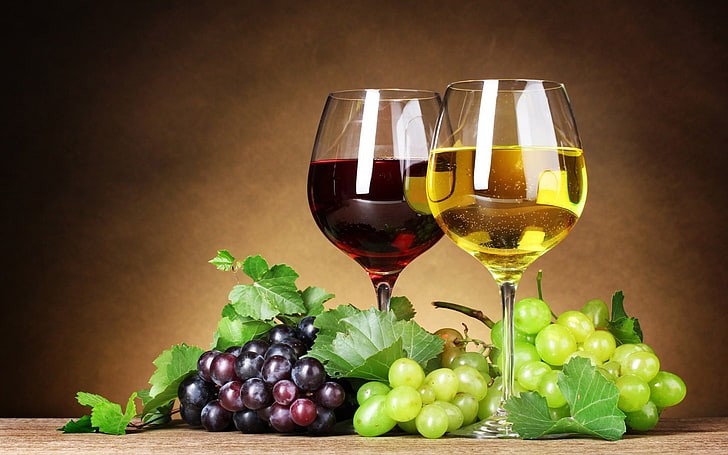 two glasses of white and red wine with two bunches of green and purple grapes