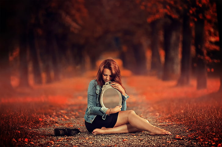 women's black skirt, woman in blue denim jacket and black mini skirt holding oval mirror sitting in the middle of pathway in forest