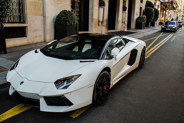 person taking photo of white Lamborghini Aventador parked near beige building during daytime