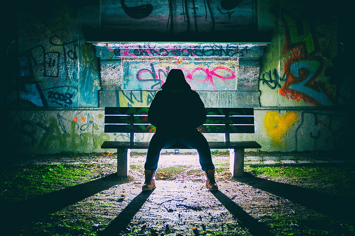 person sitting on bench behind graffiti wall, dark, selfie, color