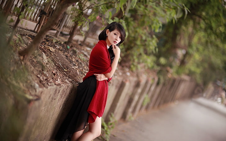 women's red cardigan, woman in red dress leaning on wall near trees