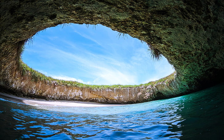 body of water with cave during daytime, beach, island, sand, grass