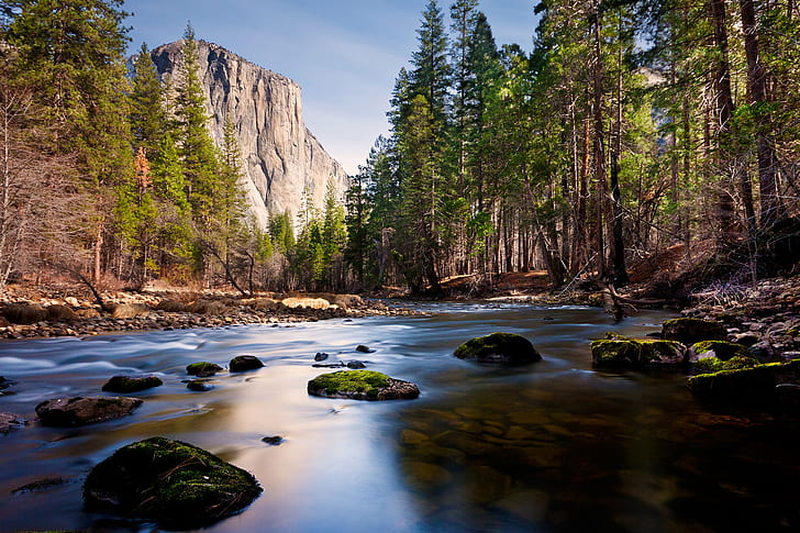 time lapse photography of flowing water in between tall trees with distance at rocky hill under blue sky, merced river, merced river