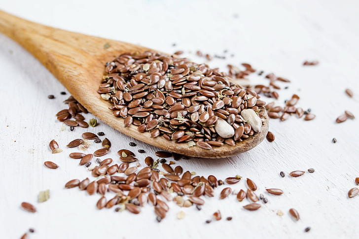 closeup photo of beans on beige wooden spatula, flax seeds, flax seeds