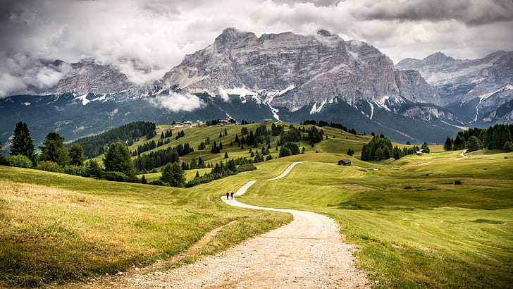 person walking on pathway between green grass field through grey mountain during daytime, alta badia, italy, alta badia, italy