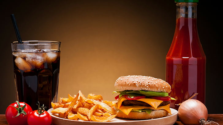 deep fried potato beside cheesy burger and two red tomato near glass of soda close-up photo
