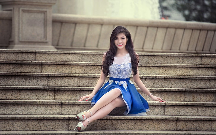 woman in white and blue floral sleeveless dress sitting on concrete stairs