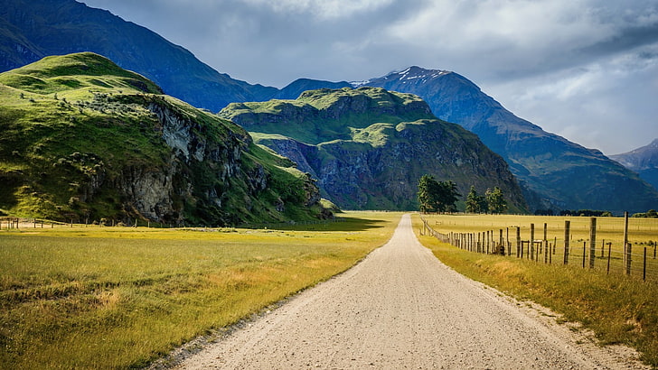 gray rough road beside green field across mountains, landscape