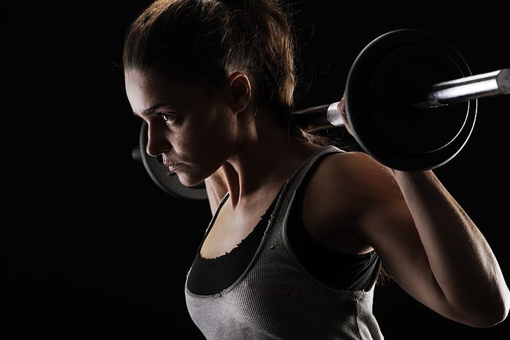 woman carrying barbell on shoulder wearing gray and black tank top