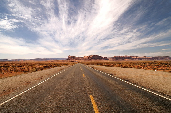 asphalt road in the middle of the desert under white clouds and blue sky during daytime