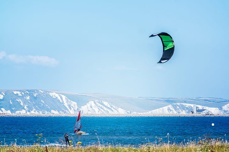 person riding water skis holding parachute near person windsurfing near the glacier mountains