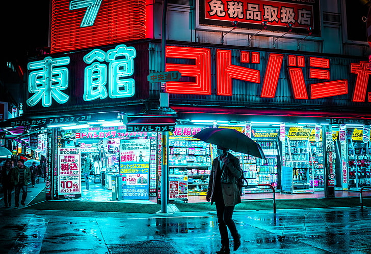 man holding umbrella walking on the street near store during nighttime