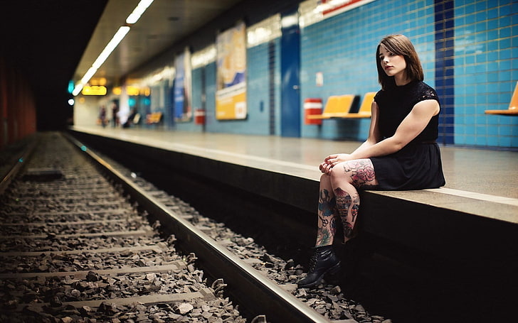 woman in black sleeveless dress sitting beside train railway