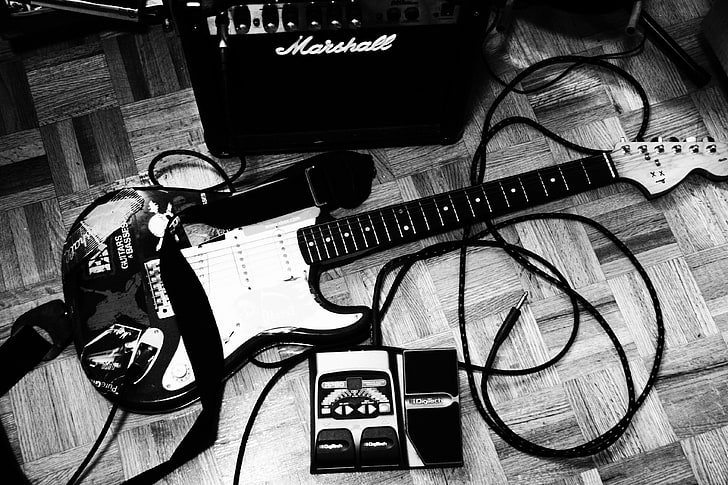 grayscale photo of stratocaster guitar besides black Marshall amplifier