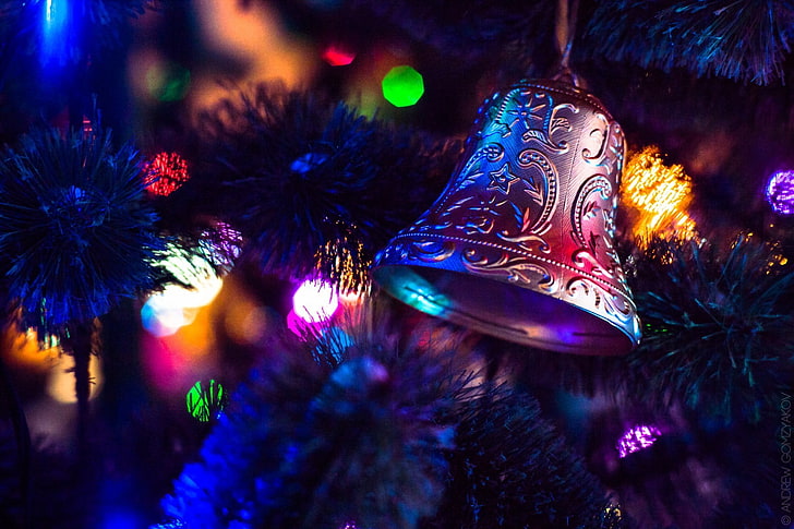 silver bell ornament, closeup photography of Christmas tree with string lights turned on