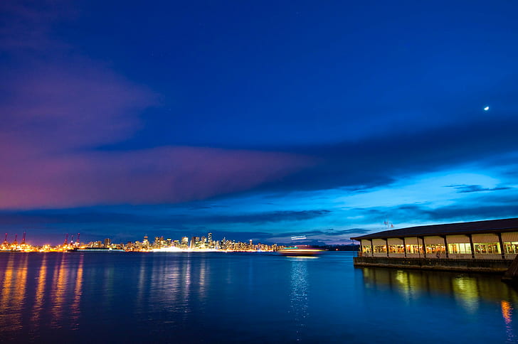 photo of lighted buildings near body of water during night, blue sea, blue sea