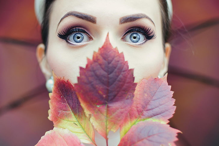 red leaves, woman with makeup on her face and brown leaf covering her nose and mouth