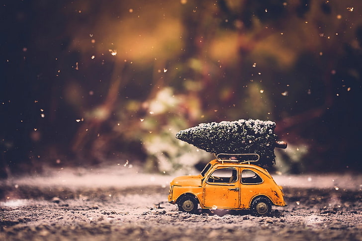 yellow car scale model, orange die-cast beetle car with pre-lit christmas tree on roof in tilt shift lens photo