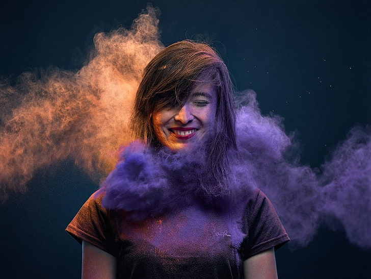 woman wearing purple cap-sleeved shirt surrounded by purple smokes while smiling landscape photography