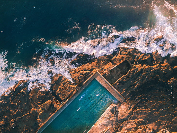 brown cliff, aerial view photography of swimming pool near sea at daytime