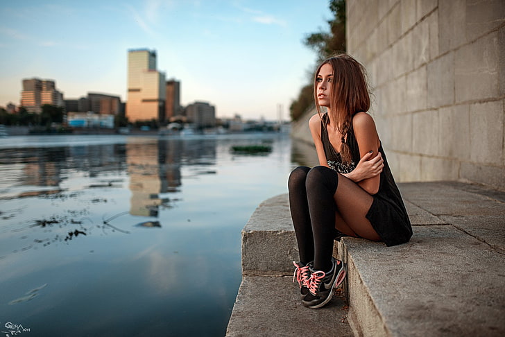 women's black sleeveless mini dress, woman wearing black top sitting on concrete stair near body of water under cloudy sky at daytime