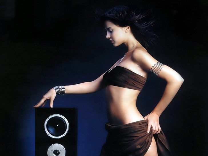 focus photo of standing woman wearing brown brassiere holding black subwoofer speaker