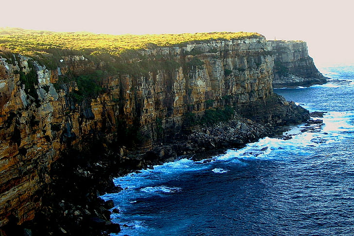 brown and gray rocky cliff beside body of water, australia, australia